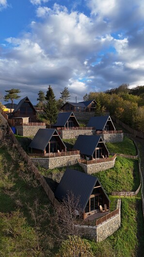 A cluster of mountain cabins with stone foundations and metal roofs, surrounded by lush greenery and trees. - ÖTÜKEN DAĞ EVLERİ (Akçaabat)