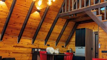 A cozy log cabin interior with a loft bedroom, a kitchen with a red refrigerator, and a dining area with red chairs.