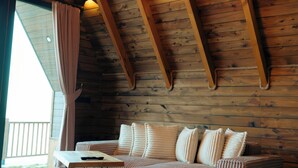 A cozy cabin interior with a wooden ceiling, a sofa with striped cushions, and hanging light fixtures. - ÖTÜKEN DAĞ EVLERİ (Akçaabat)