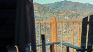 A wooden deck with a hot tub, a wooden railing, and a view of a mountainous landscape. - ÖTÜKEN DAĞ EVLERİ (Akçaabat)
