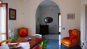 A dining area with a wooden table, chairs, and a mirror above. There is a radiator, a lamp, and a framed picture on the wall. - Villa Ninì Accommodation Salerno (Campania)