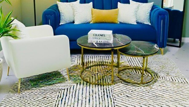A living room with a blue sofa, a white armchair, a round coffee table, and a large abstract painting on the wall. - Naivasha Budget Suites  (Naivasha)