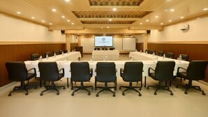 Μια αίθουσα συνεδριάσεων με ένα μεγάλο τραπέζι, μαύρες καρέκλες, μια οθόνη προβολέα και έναν λευκό πίνακα.