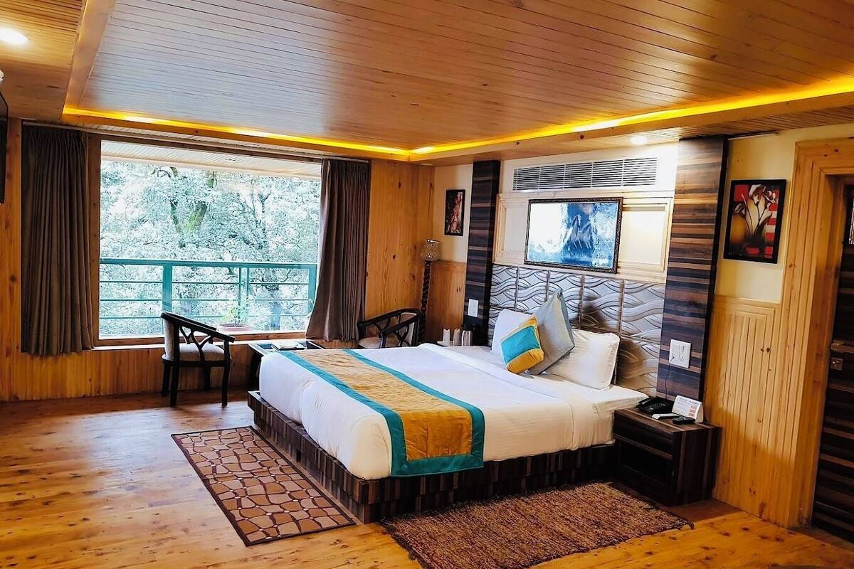A wooden-floored bedroom with a bed, bedside table, and a window with curtains.