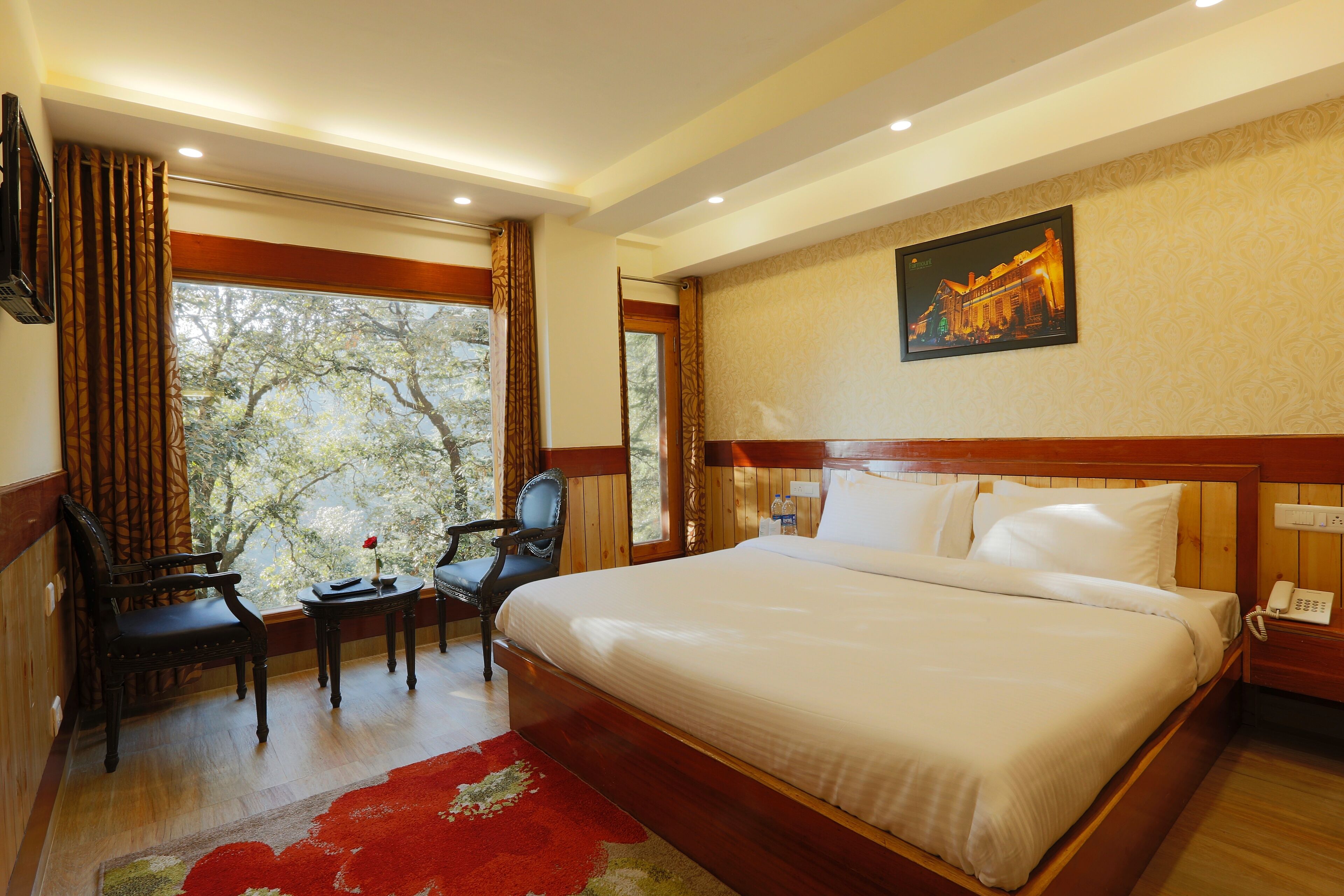 Habitación de hotel con una cama grande, un escritorio con silla, una mesita con un florero y una ventana con cortinas.
