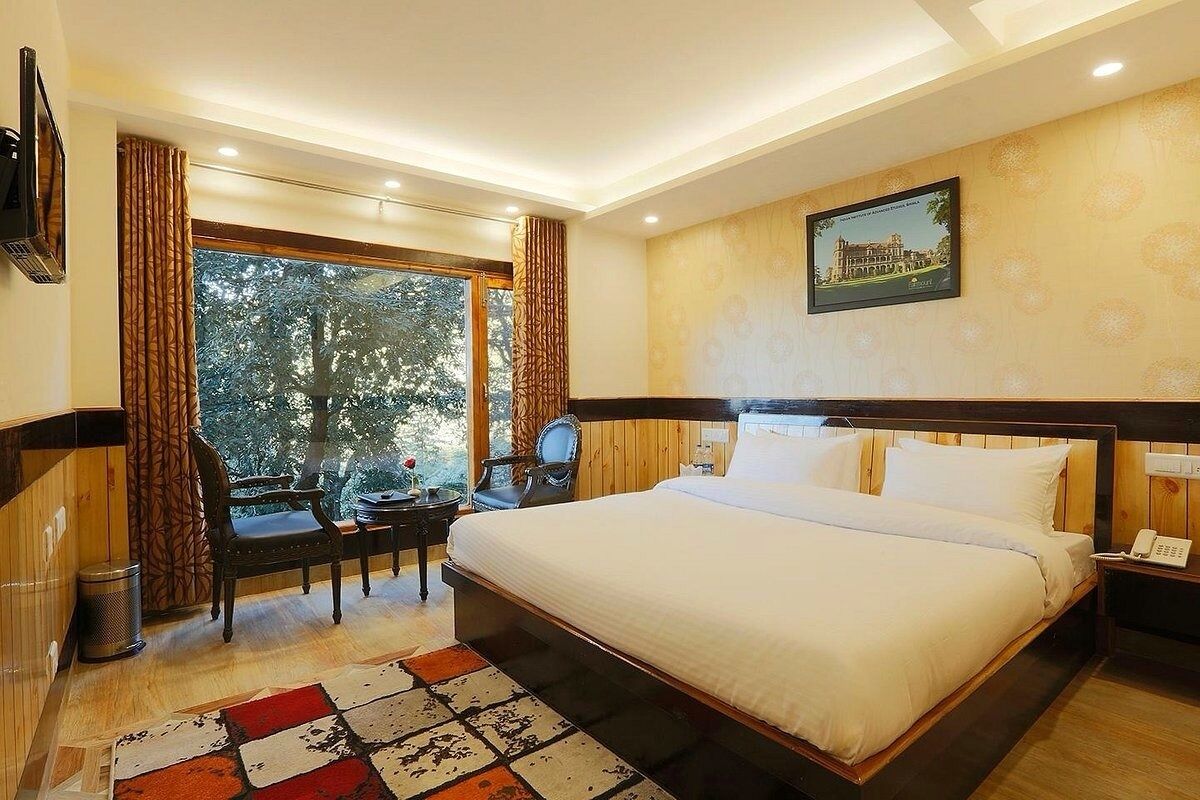 Une chambre d’hôtel avec un grand lit, un bureau avec une chaise, une fenêtre avec des rideaux et un tableau au mur.