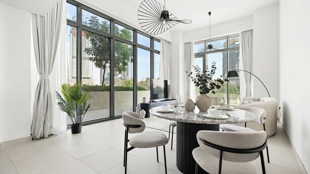 A modern dining area with a round table, four chairs, a potted plant, and a large window with a city view. - 2BR plus M Pet-Friendly Prime Amenities (Dubai)