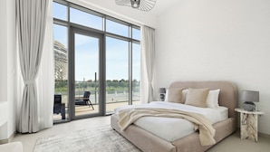 A modern bedroom with a large bed, a side table with a lamp, and a view of a balcony with a chair. - 2BR plus M Pet-Friendly Prime Amenities (Dubai)