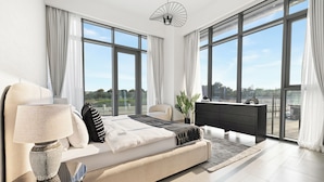 A modern bedroom with a large bed, a desk, and a view of the outdoors through large windows. - 2BR plus M Pet-Friendly Prime Amenities (Dubai)