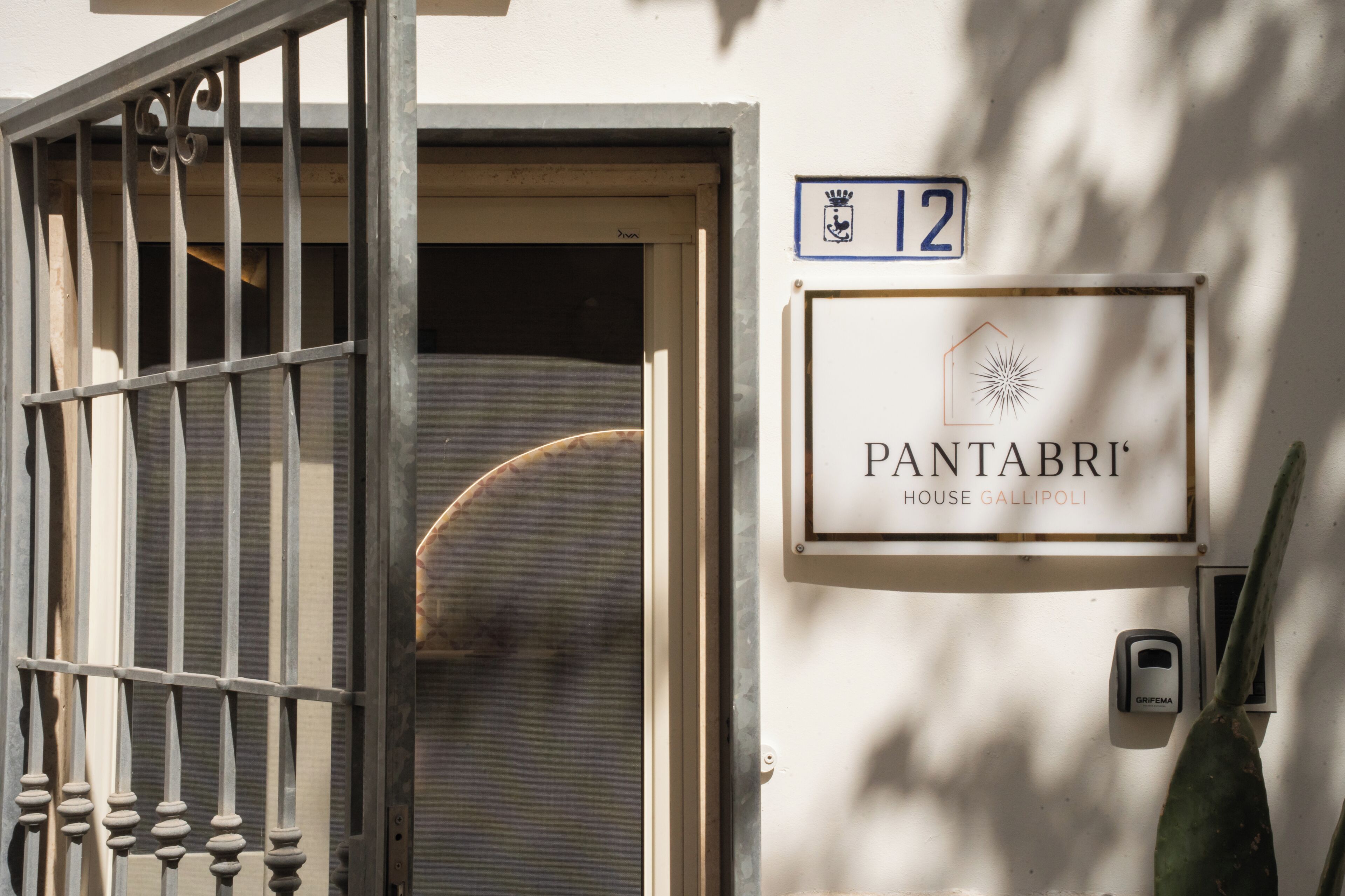 L'ingresso di un edificio con un cancello metallico, una porta e un cartello che indica 'PANTABRI HOUSE GALLIPOLI' con il numero '12' sopra.