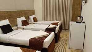 Une chambre d’hôtel avec trois lits, un petit réfrigérateur et un téléviseur fixé au mur.