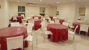 Une grande salle avec de nombreuses tables rondes recouvertes de nappes rouges et des chaises blanches.