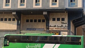 Un autobus vert est garé devant un immeuble doté de nombreuses fenêtres et d’une enseigne indiquant l’hôtel Nayer Alosoul.