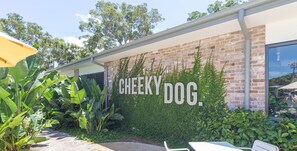 A building with a brick facade and a large sign that reads "CHEEKY DOG." - Costas Smerelda 8, 16 Soldiers Point Rd - Linen, Views, Air Con, Wi-Fi (Soldiers Point)