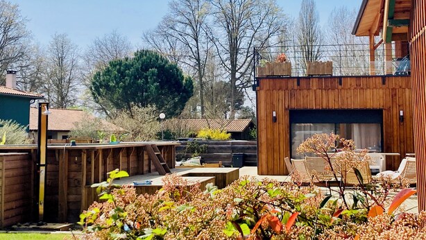 A wooden deck with outdoor seating, a barbecue area, and a large tree in the background.