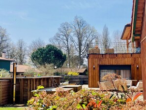 Eine Holzterrasse mit Sitzgelegenheit im Freien, einem Grillplatz und einem großen Baum im Hintergrund.