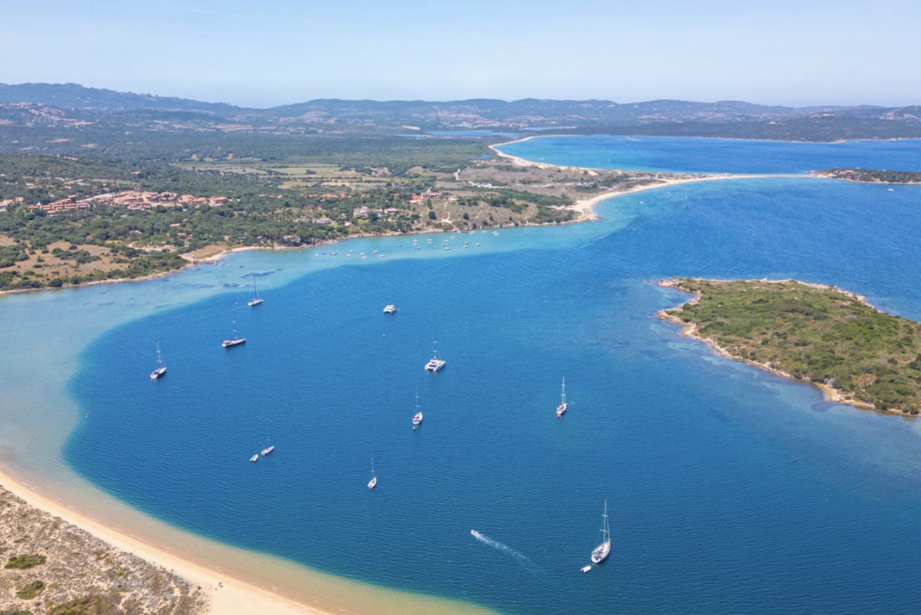 Luftaufnahme einer Küstenregion mit klarem, blauem Wasser, mehreren Booten und einem Sandstrand.