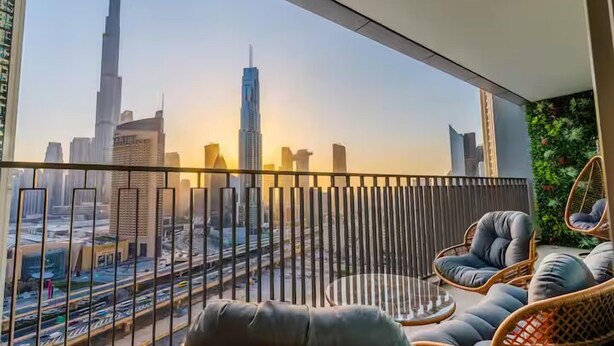 Ein Balkon mit Korbmöbeln und Blick auf eine Stadtansicht, darunter ein hoher Wolkenkratzer.