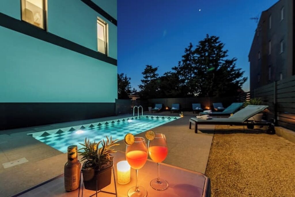 Un espace aménagé au bord de la piscine, comprenant une piscine, des chaises longues et une table avec des boissons et des bougies.