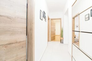 A hallway with wooden flooring, white walls, and framed pictures. There is a door leading to another room with a plant and a small table. - Villa Isola apartments 1 (Novalja)
