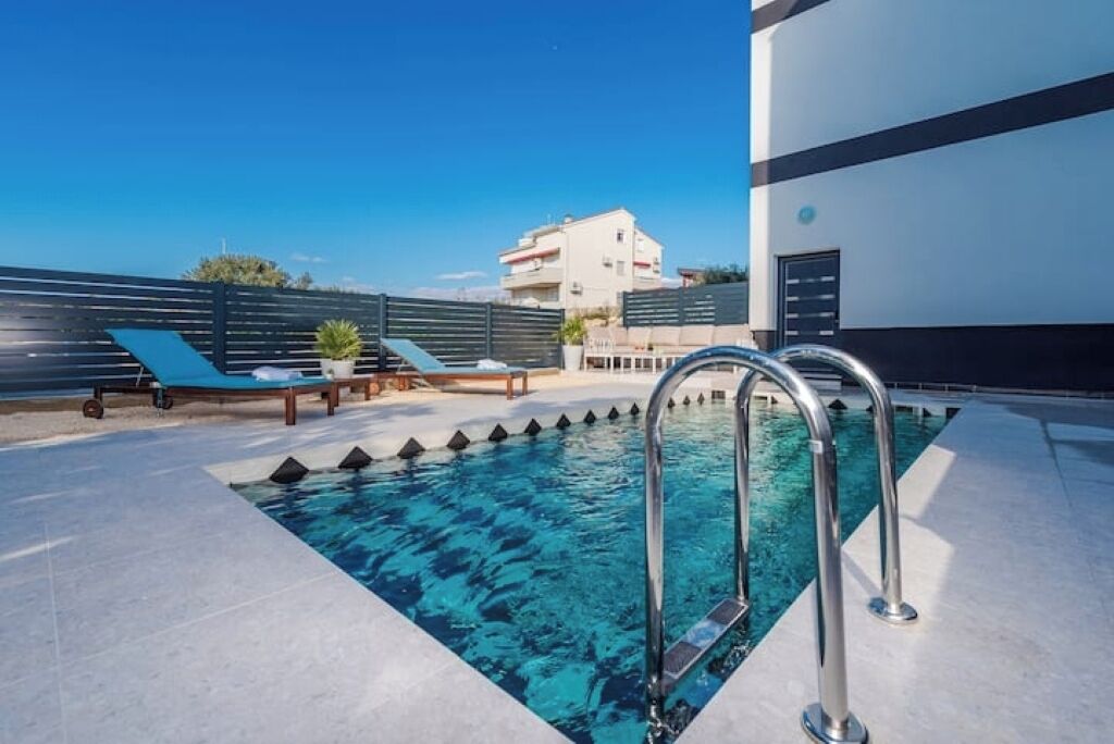 A rooftop pool with a clear blue pool, two lounge chairs, and a metal ladder.