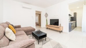 Ein modernes Wohnzimmer mit einer Couch, einem Couchtisch, einem Fernseher und einem Küchenbereich im Hintergrund.