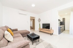 A modern living room with a sofa, coffee table, TV, and a kitchen area in the background. - Villa Isola apartments 1 (Novalja)