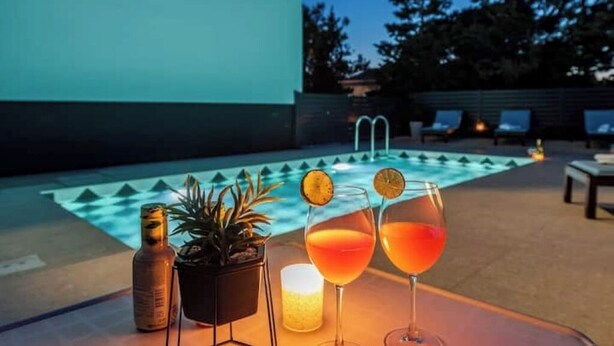 Ein Poolbereich mit einem Tisch, auf dem zwei Gläser mit rotem Getränk, eine Flasche und eine Kerze stehen.