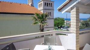 Een balkon met een tafel en stoelen, een palmboom en uitzicht op een gebouw met een klokkentoren.