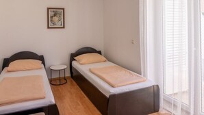 Een kleine, schone kamer met twee enkele bedden, een tafeltje en een raam met jaloezieën.