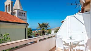 A balcony with a white table and chairs, a view of a church with a bell tower, and a clear blue sky. - Apartment Luce 2 (Povljana)