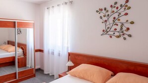 A hotel room with a bed, a wardrobe, a mirror, a window with curtains, and a wall decoration. - Apartment Luce 2 (Povljana)