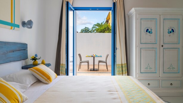 A bedroom with a bed, a wardrobe, and a view of an outdoor patio with a table and chairs. - B&B Turchese House: Asia Room (Tortolì)