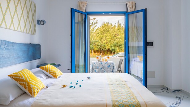 Un dormitorio con cama, almohadas, una mesita de noche, ventana con cortinas y vistas al exterior.