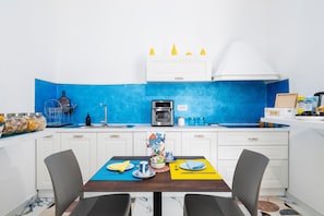 A modern kitchen with white cabinets, a blue backsplash, and a dining area with a table set for two.