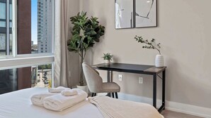 Et hotelværelse med en seng, et skrivebord, en stol, en potteplante og udsigt til byen.
