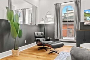Ein modernes Wohnzimmer mit Ledersessel, einer großen Pflanze und Blick auf einen Balkon mit Vorhängen.