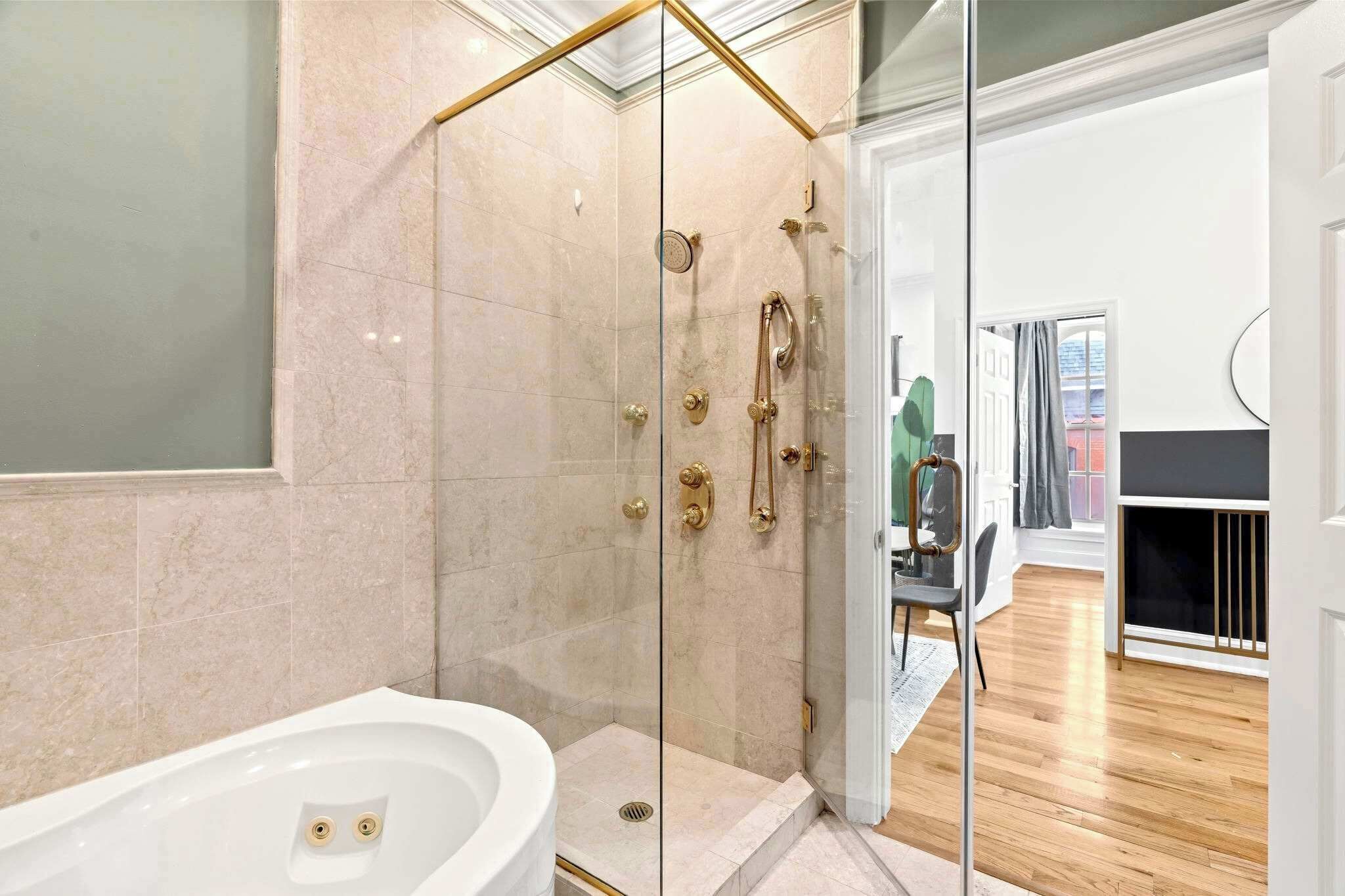 Un baño moderno con ducha de vidrio, una bañera blanca y una puerta visible que da a otra habitación.