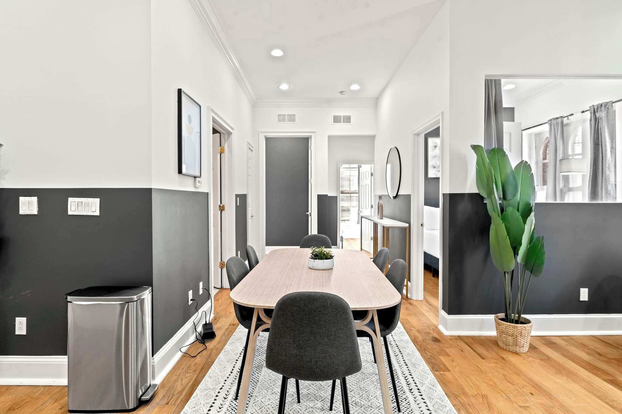 A modern dining area with a round table, chairs, a potted plant, and a trash bin.