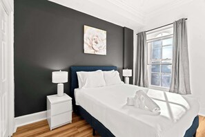 Hotellihuone, jossa on sänky, kaksi yöpöytää, ikkuna verhoilla ja taulu seinällä.