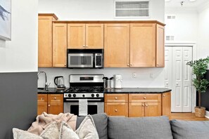 A compact kitchen with wooden cabinets, a microwave, stove, and a coffee maker. - Charming 4BR | Fits 10 | in Historic Old City PA (Philadelphia)