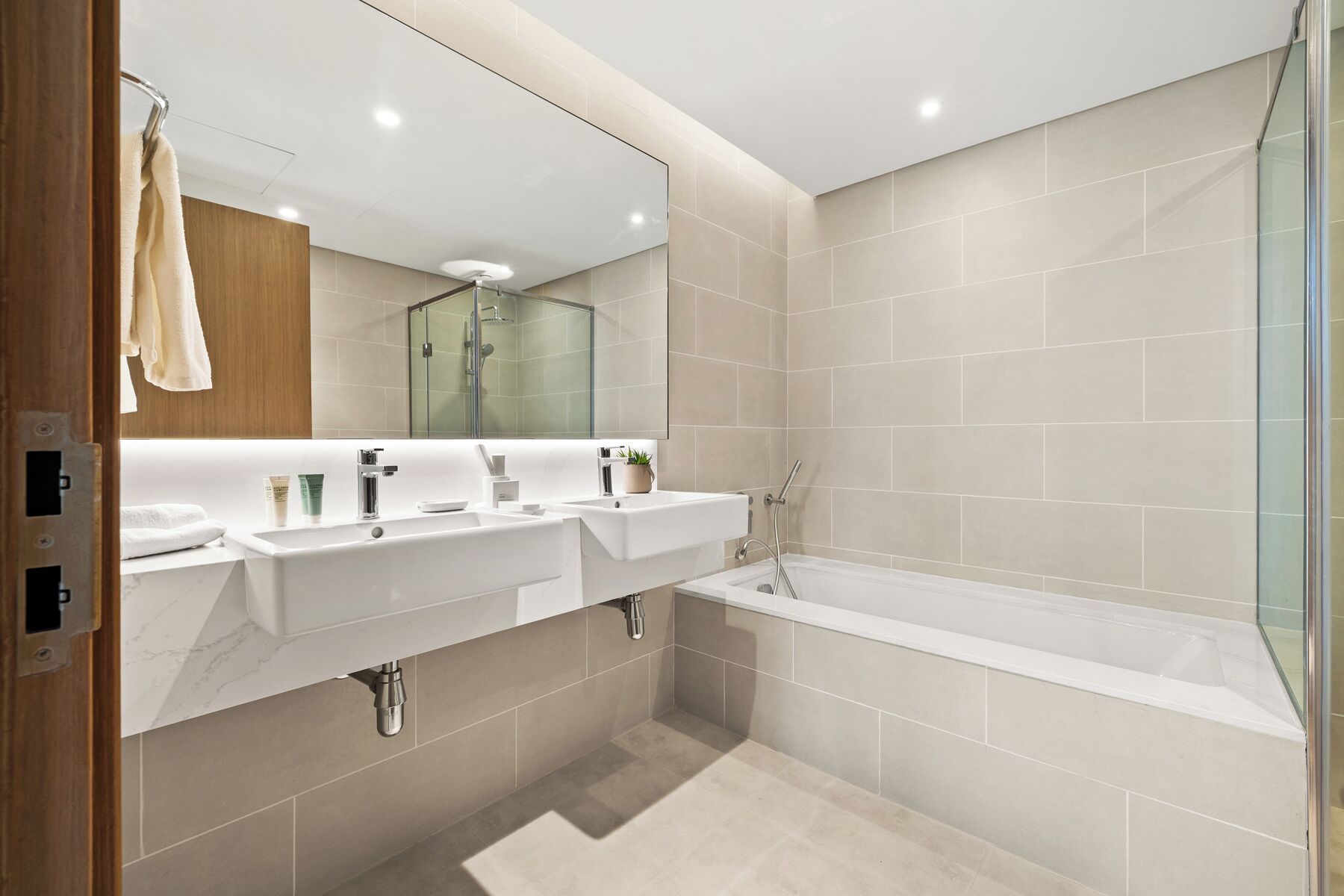A modern bathroom with two sinks, a bathtub, and a glass shower enclosure.