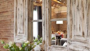 Een rustiek interieur met zichtbare bakstenen muren, een raam met houten kozijn en een eethoek die door het raam zichtbaar is.