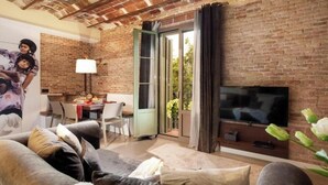 Een woonkamer met een bakstenen muur, een flatscreen televisie, een bank en een eethoek met een tafel en stoelen.