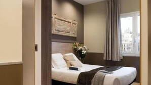 Een hotelkamer met een bed, een raam met gordijnen, een vaas met bloemen en een paar schoenen op de vloer.