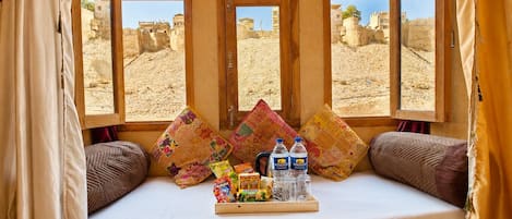 A room with a bed, pillows, a tray with snacks and drinks, and windows with desert views.