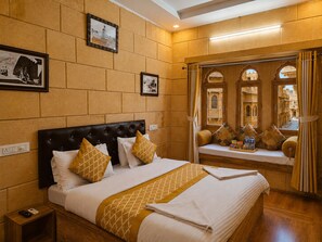 A hotel room with a large bed, a bedside table with a phone, and a window with a view of traditional architecture. - Hotel Jaswant Palace (Jaisalmer)