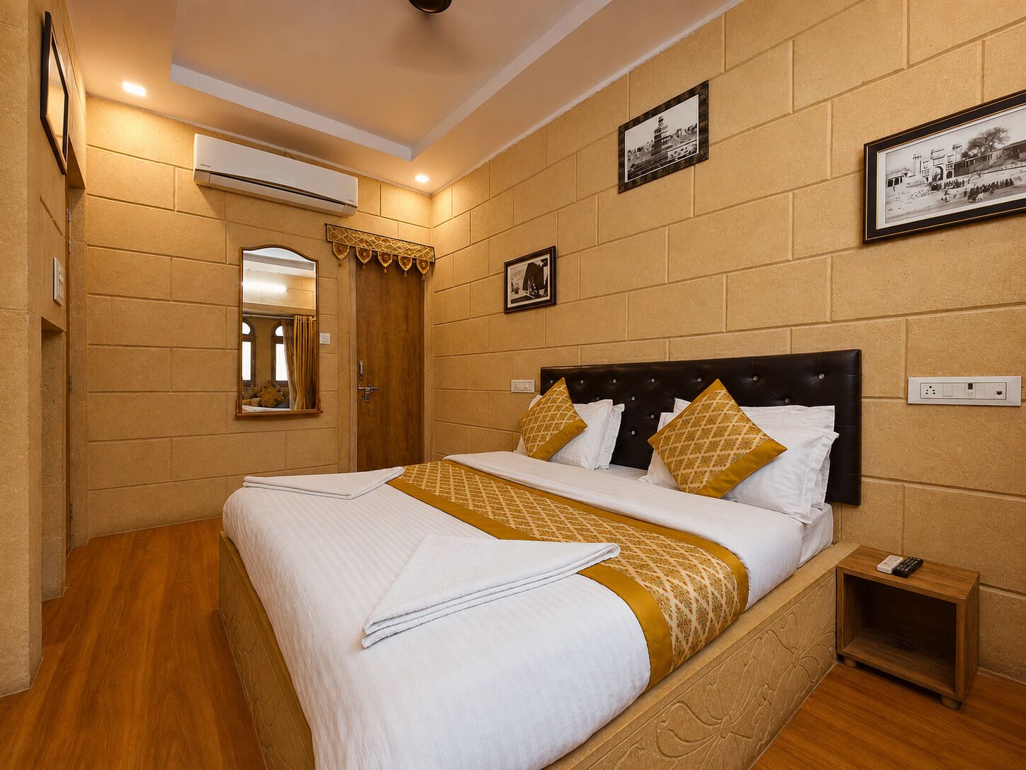 Une chambre d’hôtel avec un grand lit, une table de chevet, un miroir et un climatiseur fixé au mur.