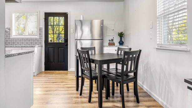 Eine moderne Küche mit einem dunklen Holzesstisch und Stühlen, einem Edelstahlkühlschrank und einem Fenster mit Jalousien.