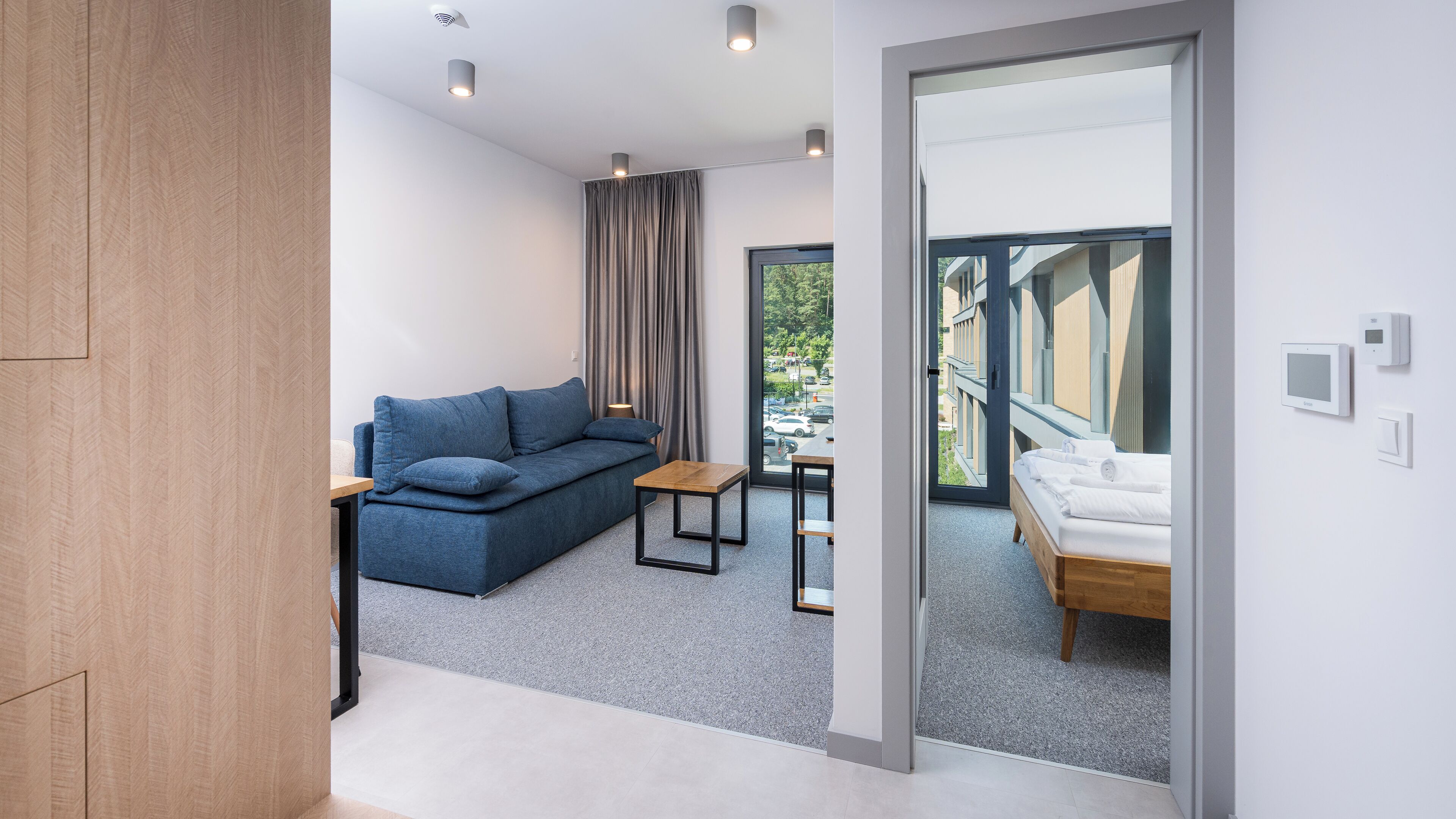A modern hotel room with a sofa, a small table, a bed, and a view of the outside.